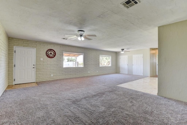 unfurnished living room with visible vents, a ceiling fan, brick wall, a textured ceiling, and carpet floors