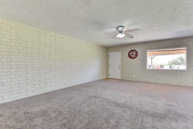 carpeted spare room featuring brick wall, ceiling fan, and a textured ceiling