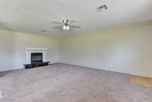 unfurnished living room with brick wall, carpet flooring, visible vents, a ceiling fan, and a glass covered fireplace