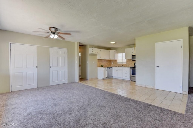 unfurnished living room with light carpet, light tile patterned floors, ceiling fan, and a textured ceiling