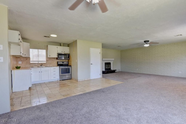 kitchen with light carpet, tasteful backsplash, a fireplace with raised hearth, white cabinets, and appliances with stainless steel finishes