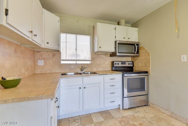 kitchen featuring a sink, white cabinetry, appliances with stainless steel finishes, tile counters, and tasteful backsplash