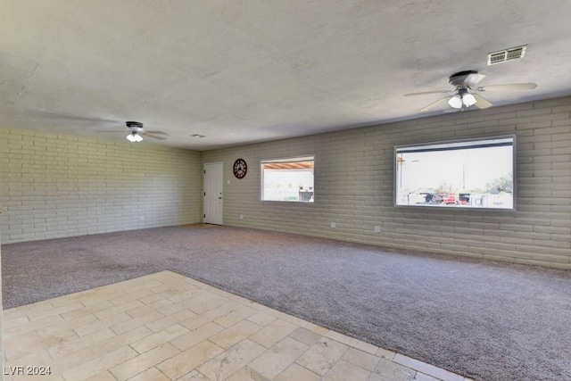 unfurnished room with brick wall, visible vents, a textured ceiling, and carpet flooring