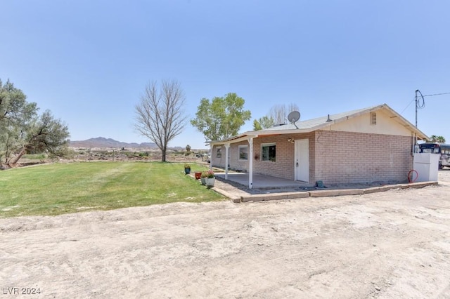 exterior space with brick siding, a mountain view, a front lawn, and a patio