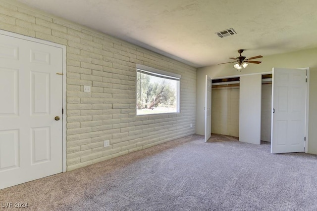 unfurnished bedroom featuring visible vents, brick wall, ceiling fan, carpet floors, and two closets