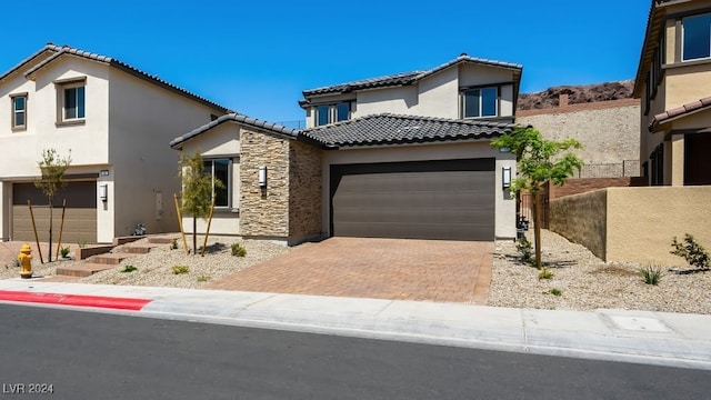 mediterranean / spanish-style house featuring stucco siding, a tiled roof, decorative driveway, stone siding, and an attached garage