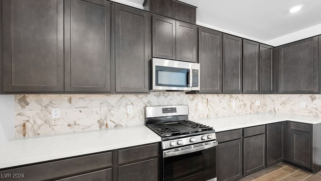 kitchen with light wood-style floors, appliances with stainless steel finishes, light countertops, dark brown cabinets, and backsplash