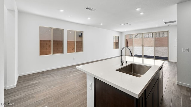 kitchen with a kitchen island with sink, light countertops, light wood finished floors, a sink, and baseboards