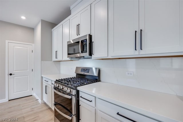 kitchen with white cabinetry, backsplash, light hardwood / wood-style flooring, and appliances with stainless steel finishes