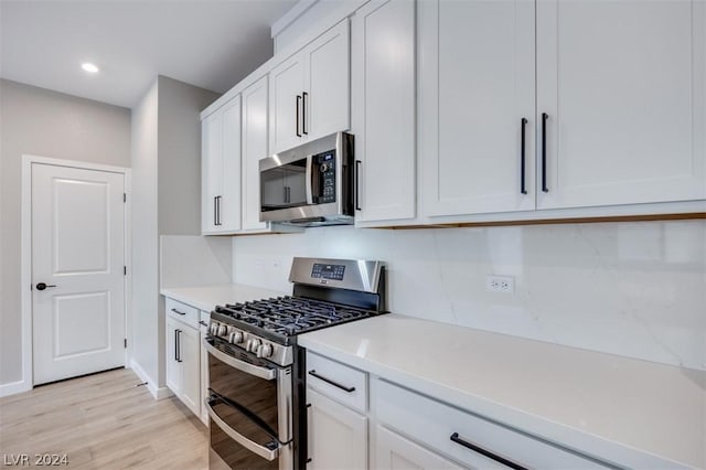 kitchen with appliances with stainless steel finishes, built in desk, light wood-type flooring, and white cabinets