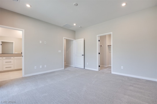 unfurnished bedroom featuring light carpet, connected bathroom, a closet, and a walk in closet