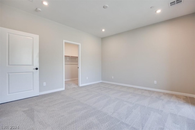 unfurnished bedroom with light carpet and a walk in closet