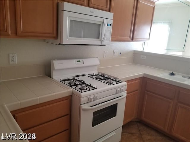 kitchen featuring sink, tile counters, dark tile patterned flooring, and white appliances