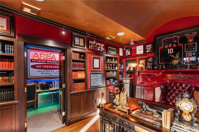 home office featuring built in shelves, lofted ceiling, visible vents, and light wood finished floors