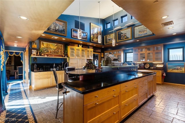 kitchen with a sink, an island with sink, dark countertops, a kitchen bar, and glass insert cabinets