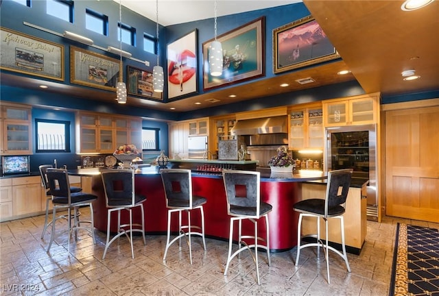 bar featuring a community bar, visible vents, a towering ceiling, wall chimney exhaust hood, and decorative light fixtures