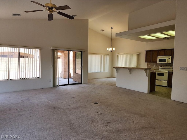 unfurnished living room with high vaulted ceiling, ceiling fan with notable chandelier, and light colored carpet