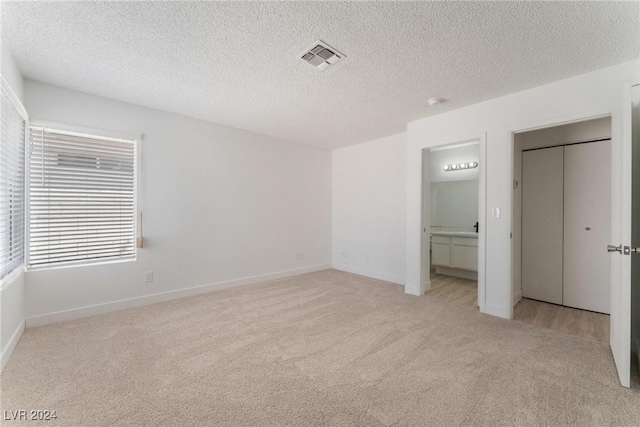 unfurnished bedroom featuring light colored carpet, ensuite bathroom, a closet, and a textured ceiling