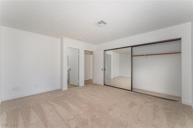 unfurnished bedroom featuring light carpet, a closet, and a textured ceiling