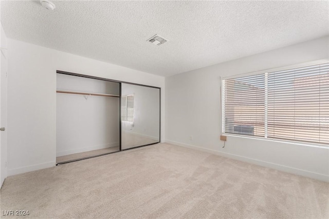 unfurnished bedroom featuring light carpet, a closet, and a textured ceiling