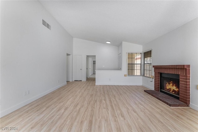 unfurnished living room with lofted ceiling, a brick fireplace, and light hardwood / wood-style flooring