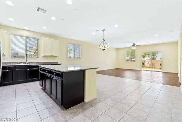 kitchen with light wood-type flooring, light stone counters, a kitchen island, ceiling fan, and decorative light fixtures