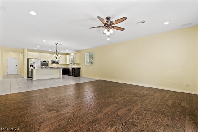 unfurnished living room with ceiling fan, a sink, visible vents, and light wood-style floors