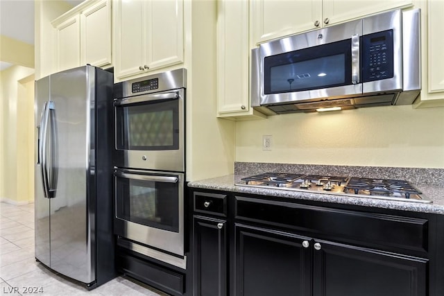 kitchen featuring white cabinets, appliances with stainless steel finishes, dark cabinets, light stone countertops, and light tile patterned flooring