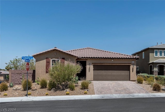 mediterranean / spanish house with a tiled roof, decorative driveway, an attached garage, and stucco siding