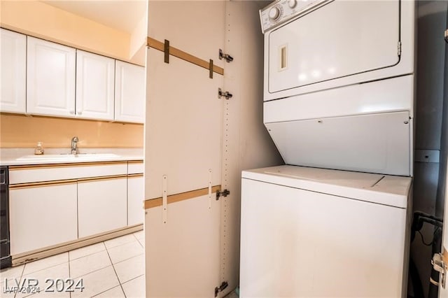 clothes washing area with sink, light tile patterned floors, and stacked washer and dryer