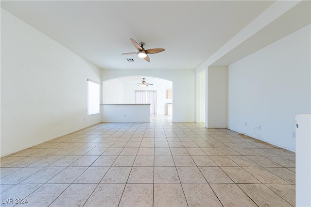 unfurnished living room with light tile patterned floors, ceiling fan, and arched walkways