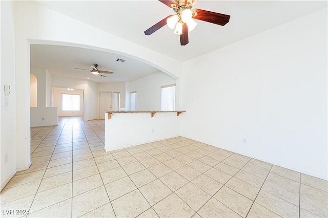 empty room with arched walkways, light tile patterned floors, visible vents, and a ceiling fan