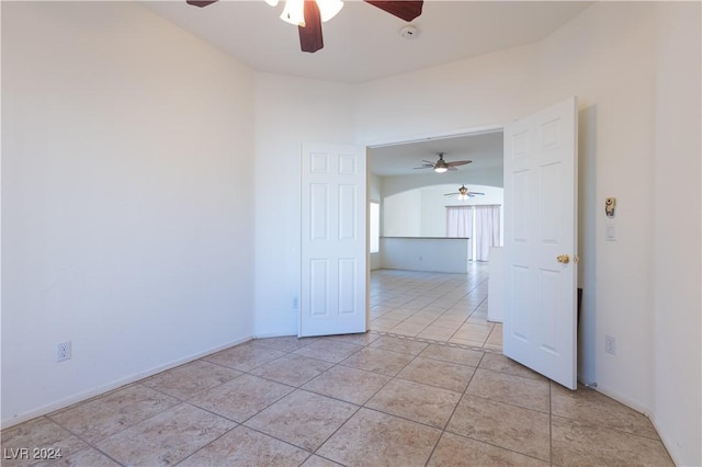 empty room with light tile patterned floors, baseboards, and a ceiling fan