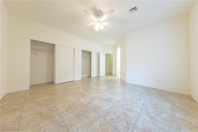 unfurnished bedroom featuring a ceiling fan, arched walkways, visible vents, and two closets