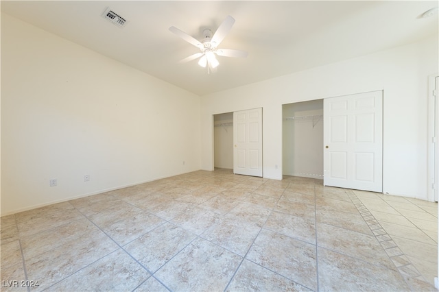 unfurnished bedroom with light tile patterned flooring, ceiling fan, and two closets