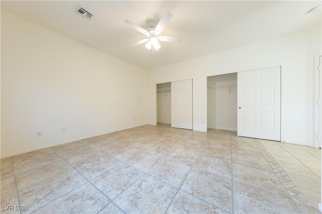 unfurnished bedroom with light tile patterned floors, visible vents, baseboards, ceiling fan, and multiple closets