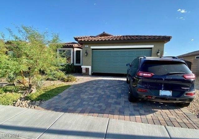 view of front of home with a tile roof, decorative driveway, a garage, and stucco siding