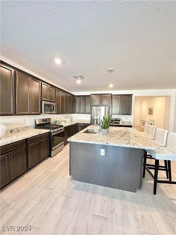 kitchen with appliances with stainless steel finishes, light stone countertops, a kitchen island with sink, and a breakfast bar area