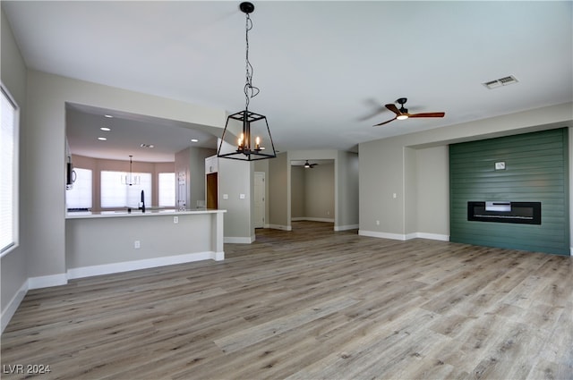 unfurnished living room featuring a large fireplace, baseboards, visible vents, light wood-style floors, and ceiling fan with notable chandelier