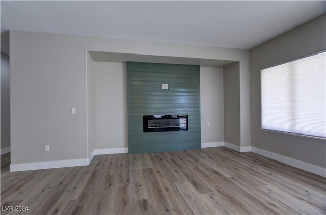 unfurnished living room featuring a large fireplace, light wood-type flooring, and baseboards