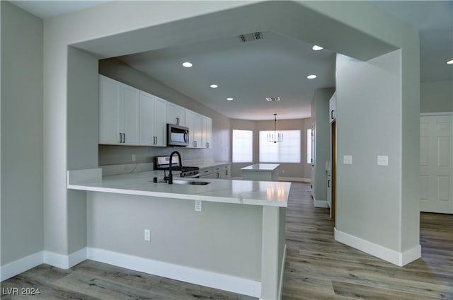 kitchen with a peninsula, stainless steel microwave, light countertops, and white cabinets