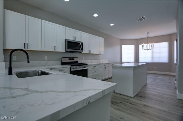 kitchen featuring white cabinets, decorative light fixtures, a center island, light stone countertops, and stainless steel appliances