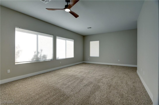 spare room featuring light colored carpet, ceiling fan, visible vents, and baseboards