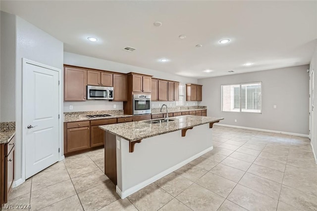 kitchen featuring sink, a breakfast bar area, appliances with stainless steel finishes, an island with sink, and light stone countertops