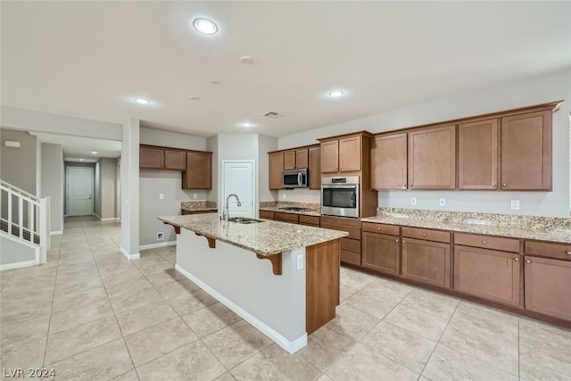 kitchen with sink, a breakfast bar area, light stone counters, a center island with sink, and stainless steel appliances