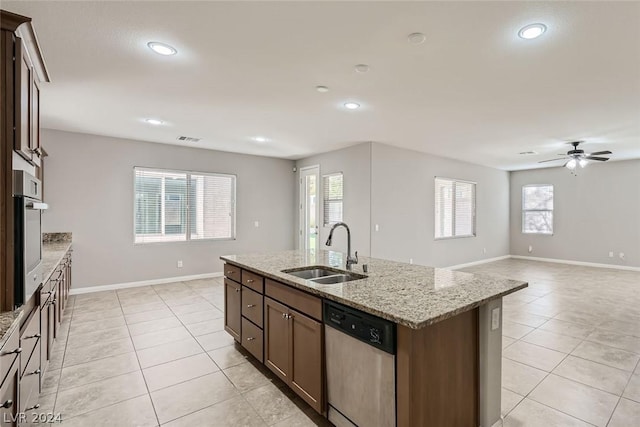 kitchen with light tile patterned flooring, appliances with stainless steel finishes, sink, light stone counters, and a center island with sink