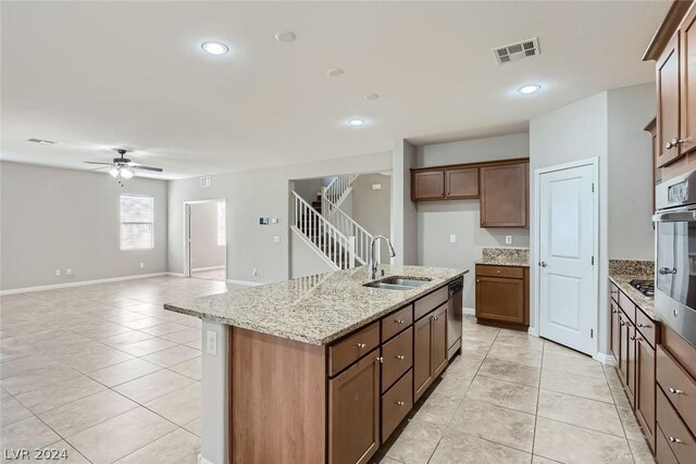 kitchen with sink, light tile patterned floors, appliances with stainless steel finishes, light stone countertops, and an island with sink