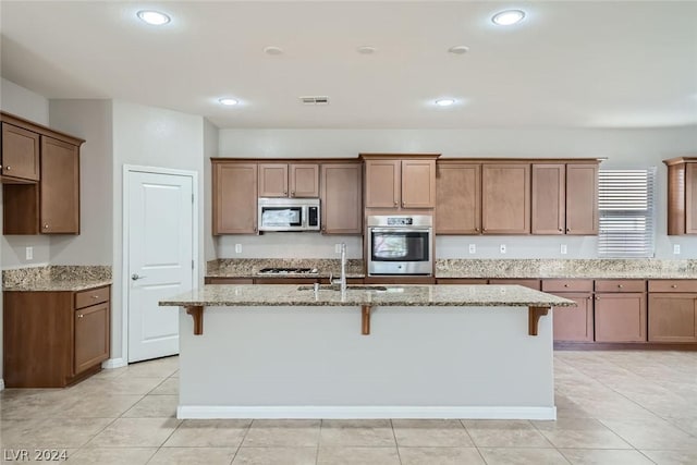 kitchen with a kitchen bar, stainless steel appliances, light stone countertops, and a center island with sink