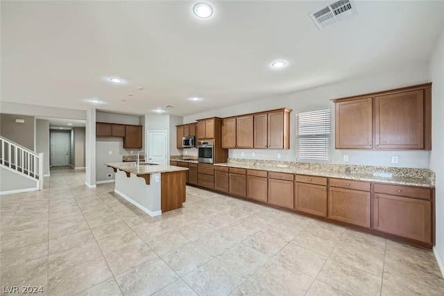 kitchen with sink, a kitchen bar, light stone counters, stainless steel appliances, and a center island with sink