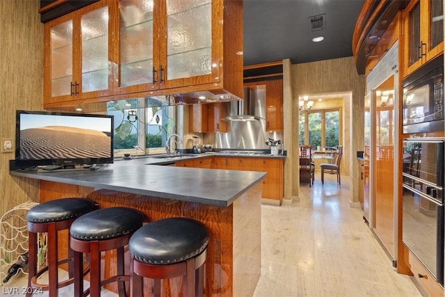 kitchen featuring a kitchen breakfast bar, kitchen peninsula, sink, and wall chimney range hood